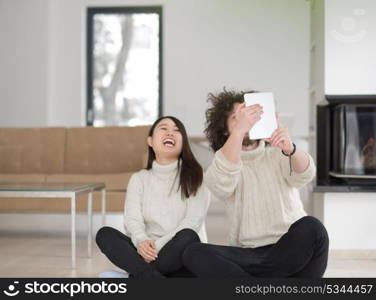 beautiful young multiethnic couple using tablet computer in front of fireplace on cold winter day at home