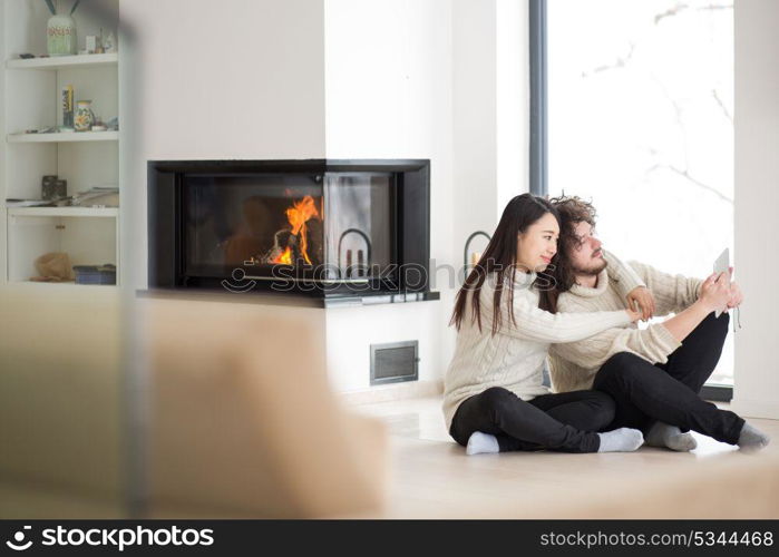 beautiful young multiethnic couple using tablet computer in front of fireplace on cold winter day at home