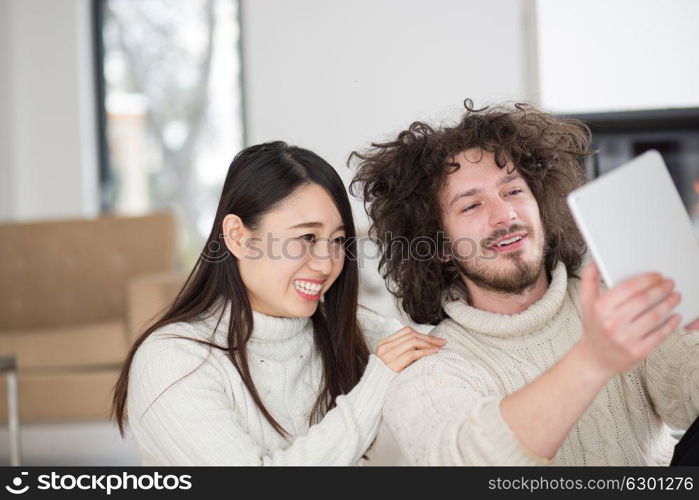 beautiful young multiethnic couple using tablet computer in front of fireplace on cold winter day at home