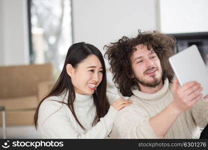 beautiful young multiethnic couple using tablet computer in front of fireplace on cold winter day at home