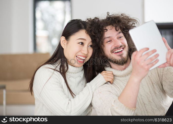 beautiful young multiethnic couple using tablet computer in front of fireplace on cold winter day at home