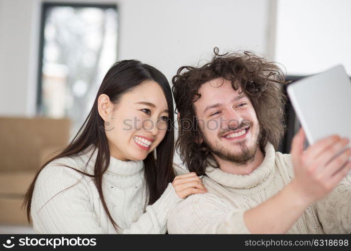 beautiful young multiethnic couple using tablet computer in front of fireplace on cold winter day at home