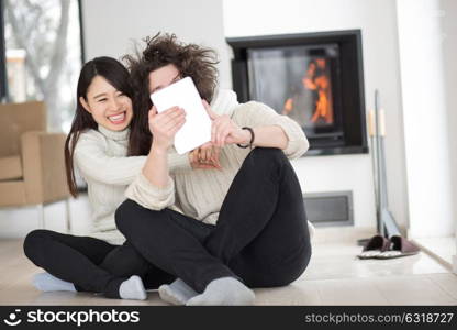 beautiful young multiethnic couple using tablet computer in front of fireplace on cold winter day at home