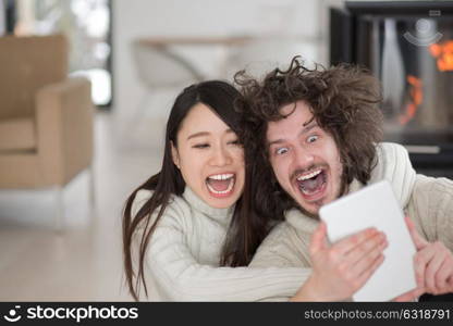 beautiful young multiethnic couple using tablet computer in front of fireplace on cold winter day at home