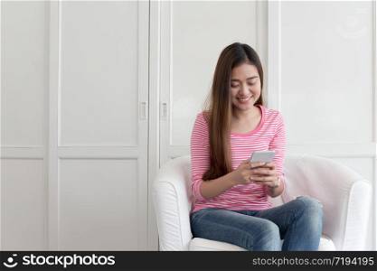 Beautiful young of Asian girl using a smartphone while sitting on the sofa in the living room at home, Asia women happy smile while chatting on mobile phone