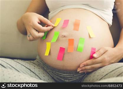 Beautiful young pregnant woman holding colorful memo stickers