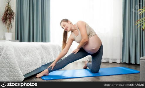 Beautiful young pregnant woman in sports outfit doing fitness exercises and stretching on sportrs mat at home. Concept of healthcare and sports during pregnancy.. Beautiful young pregnant woman in sports outfit doing fitness exercises and stretching on sportrs mat at home. Concept of healthcare and sports during pregnancy