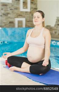 Beautiful young pregnant woman sitting with legs crossed on fitness mat