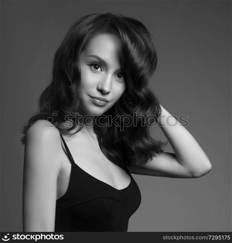beautiful young pretty lady in black dress. Classic portrait of woman with stylish hair-dressing. Sexy caucasian model with black hair pose in photography studio on grey background