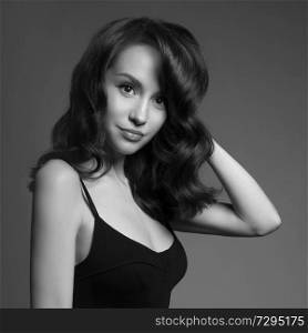 beautiful young pretty lady in black dress. Classic portrait of woman with stylish hair-dressing. Sexy caucasian model with black hair pose in photography studio on grey background