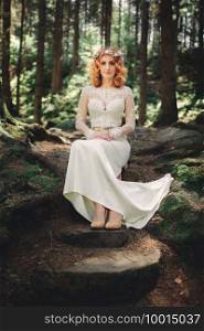 beautiful young red-haired bride in the forest with a floral wreath on her head. woman in long white dress outdoors on summer day. wedding day.. beautiful young red-haired bride in the forest with a floral wreath on her head. woman in long white dress outdoors on summer day. wedding day