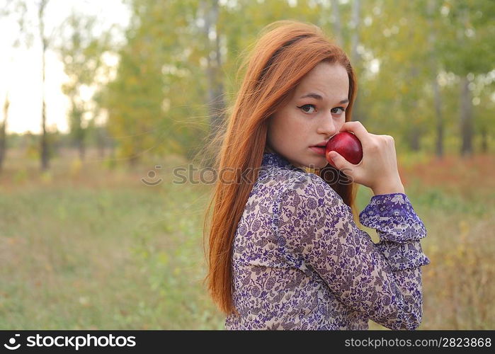 Beautiful young redhead in a autumn meadow with red apple