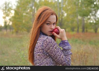 Beautiful young redhead in a autumn meadow with red apple