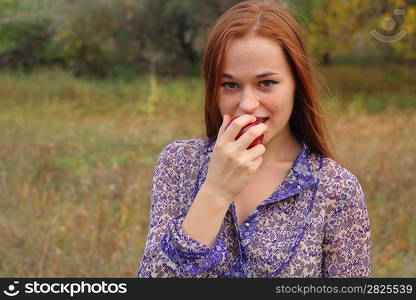 Beautiful young redhead in a autumn meadow with red apple