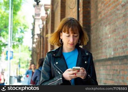 beautiful young redhead woman sending message with smartphone on the street.
