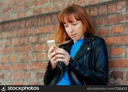 beautiful young redhead woman sending message with smartphone on the street.