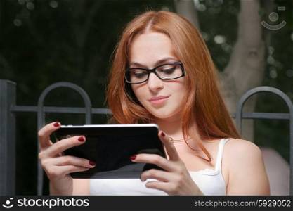 Beautiful young redhead woman with a tablet-pc in the park leaning using the touchscreen. Redhead woman with tablet outdoors