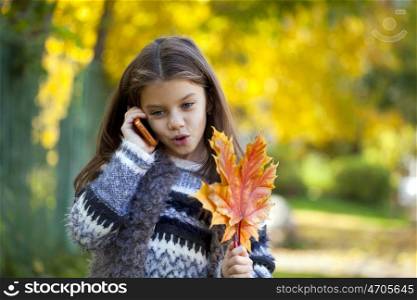 Beautiful young school girl talking on mobile phone in the autumn park