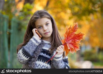 Beautiful young school girl talking on mobile phone in the autumn park