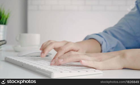 Beautiful young smiling Asian woman working on laptop while at home in office work space. Businesswoman working from home via portable computer writing on keyboard. Enjoying time at home.