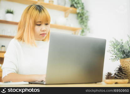 Beautiful young smiling Asian woman working on laptop while at home in office work space. Businesswoman working from home via portable computer writing on keyboard. Enjoying time at home.