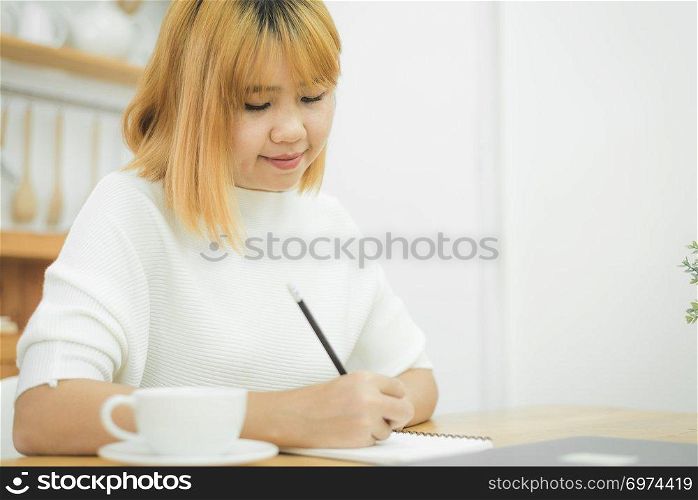 Beautiful young smiling asian woman working on laptop while sitting in a living room at home. Asian business woman working in her home office. Enjoying time at home.