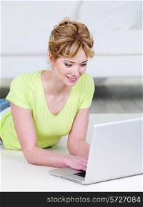 Beautiful young smiling woman in casuals lying and using laptop - indoors