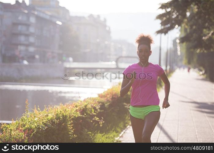 Beautiful young sporty african american woman running at early morning jogging with city sunrise scene in background