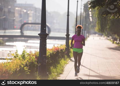 Beautiful young sporty african american woman running at early morning jogging with city sunrise scene in background