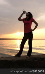 Beautiful young sporty woman drinking in front of a sunset.
