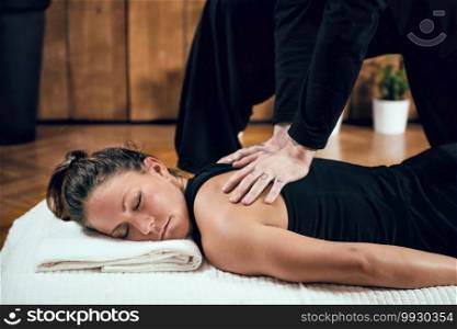 Beautiful young sporty woman enjoying shiatsu back massage, lying on the wooden floor, wearing black top