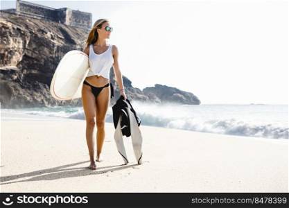 Beautiful young surfer girl walking on the beach
