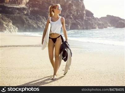 Beautiful young surfer girl walking on the beach
