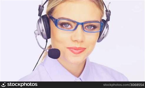 Beautiful young telesales lady wearing glasses and and a headset working at her laptop computer turning to smile at the camera