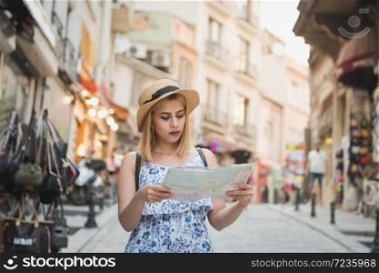 Beautiful young tourist girl in fashionable clothes with map walks around at street and explores city in summer season.Traveler Concept image. Beautiful girl explores streets of city with map