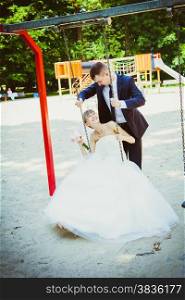 beautiful young wedding couple in park, blonde bride on swing and her groom