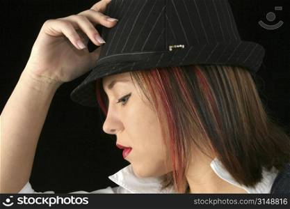 Beautiful young woman&acute;s profile putting on hat. Shot in studio over black.
