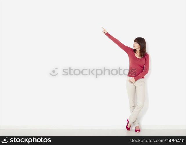 Beautiful young woman against to a white wall pointing to the right side with copyspace