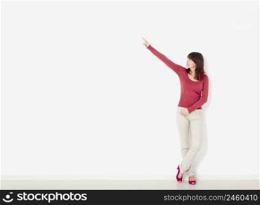 Beautiful young woman against to a white wall pointing to the right side with copyspace