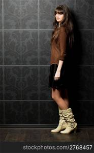 beautiful young woman against wall with pattern, standing sideways, full body