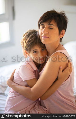 Beautiful young woman and her charming little daughter are hugging on the bed.. Beautiful young woman and her charming little daughter are hugging.