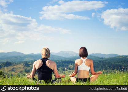 Beautiful young woman and man doing yoga exercise at the summer meadow