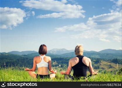 Beautiful young woman and man doing yoga exercise at the summer meadow