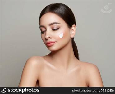 Beautiful young woman applying cosmetic cream treatment on her face isolated on background . Girl with clean fresh skin. Cosmetology and spa