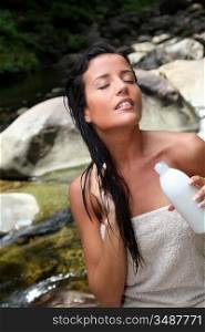 Beautiful young woman applying hair conditioner sitting by river