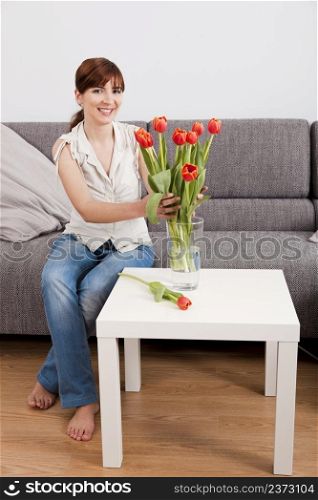 Beautiful young woman at home making an arrangement of orange tulips