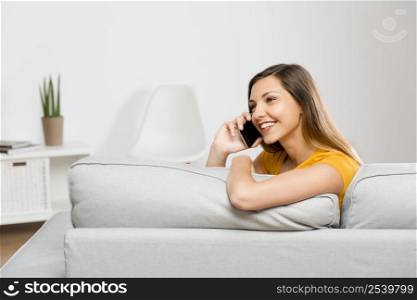 Beautiful young woman at home sitting on sofa and talking at phone
