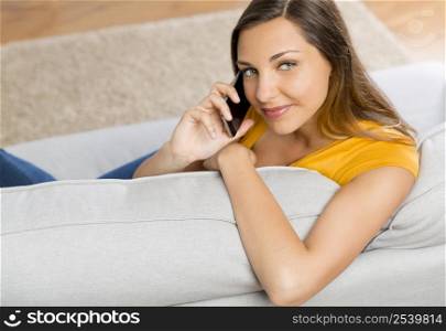 Beautiful young woman at home sitting on sofa and talking at phone