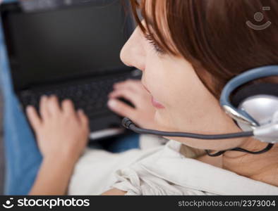 Beautiful young woman at home with a laptop and speaking over the internet with headphones