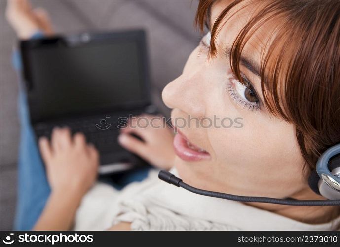Beautiful young woman at home with a laptop and speaking over the internet with headphones